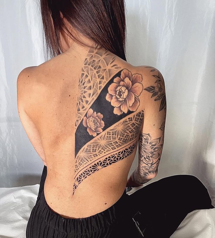 Intricate floral and geometric tattoo on woman's back, showcasing detailed artistry and design on skin.