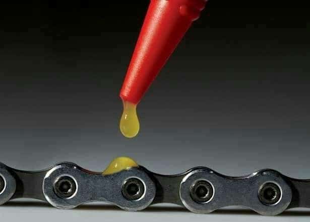 Applying lubricant to a bicycle chain with a red nozzle for smooth performance and maintenance.