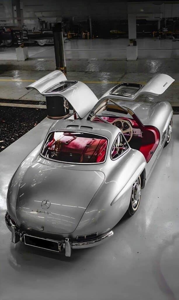 92c9b0d8f0de227b233a98d6d59b5414 Silver classic Mercedes-Benz 300SL with gullwing doors open, showcasing red interior, parked indoors on a shiny floor. | Sky Rye Design Silver classic Mercedes-Benz 300SL with gullwing doors open, showcasing red interior, parked indoors on a shiny floor.