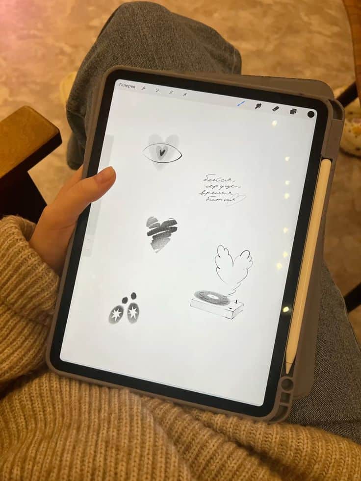 93cbd075534f77648211c06e6e4a3617 Person sketching creative doodles on iPad with stylus, featuring an eye, heart, and abstract designs, in cozy setting. | Sky Rye Design Person sketching creative doodles on iPad with stylus, featuring an eye, heart, and abstract designs, in cozy setting.