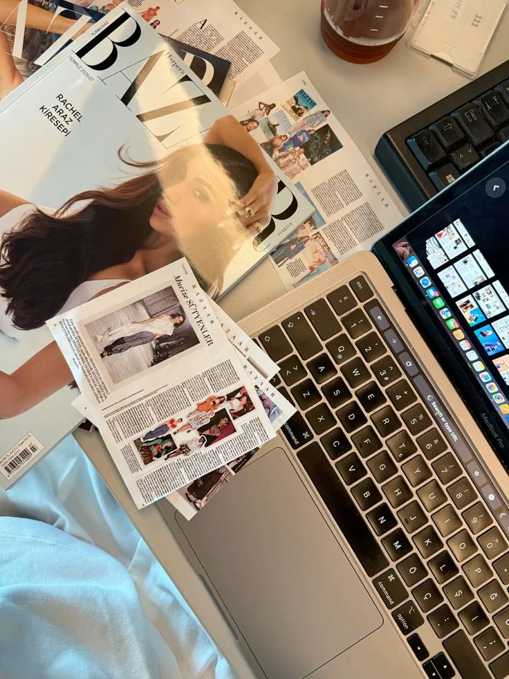 Fashion magazines and a laptop on a desk, highlighting a workspace for digital content creation and style inspiration.