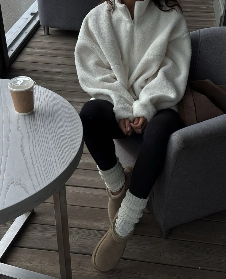 Cozy cafe scene with person wearing a fluffy white pullover and sipping coffee, sitting comfortably in a modern chair.