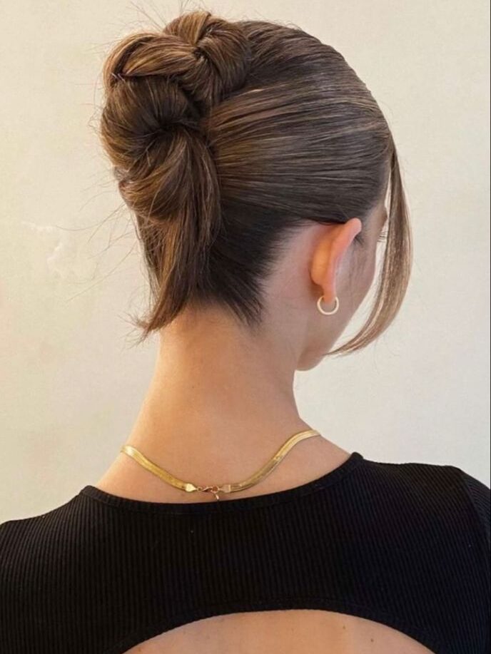 Elegant woman with intricate updo, wearing a black backless dress and hoop earring, showcasing stylish fashion.