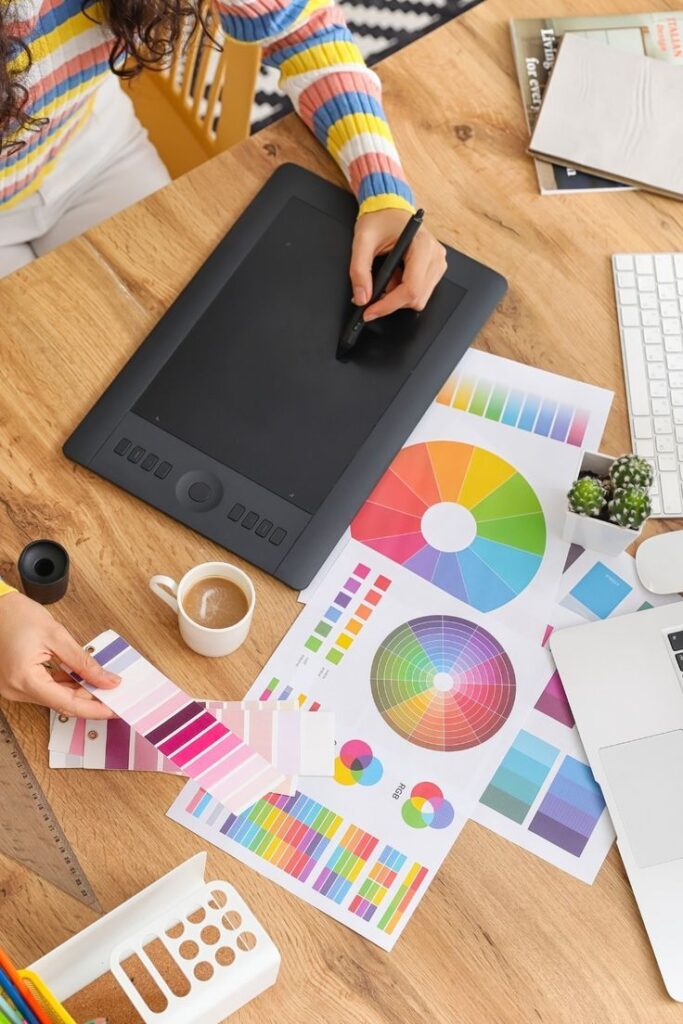 Designer working with graphics tablet, color swatches, and charts on desk for creative design project.
