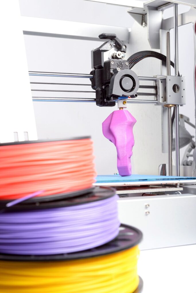 3D printer in action with purple filament, surrounded by colorful spools, demonstrating modern manufacturing technology.