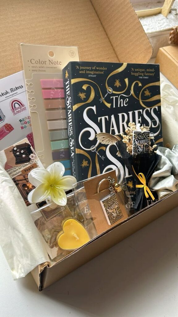 9e8d5727-61cf-4a7d-b105-89ecba7a2f20 Gift box with The Starless Sea book, sticky notes, decorative items, and a heart-shaped candle, creating a cozy reading experience. | Sky Rye Design Gift box with The Starless Sea book, sticky notes, decorative items, and a heart-shaped candle, creating a cozy reading experience.