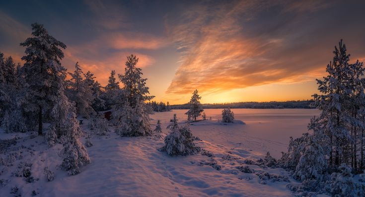 Snow-covered landscape at sunrise with a vibrant sky, trees, and a frozen lake. Peaceful winter scenery perfect for nature lovers.