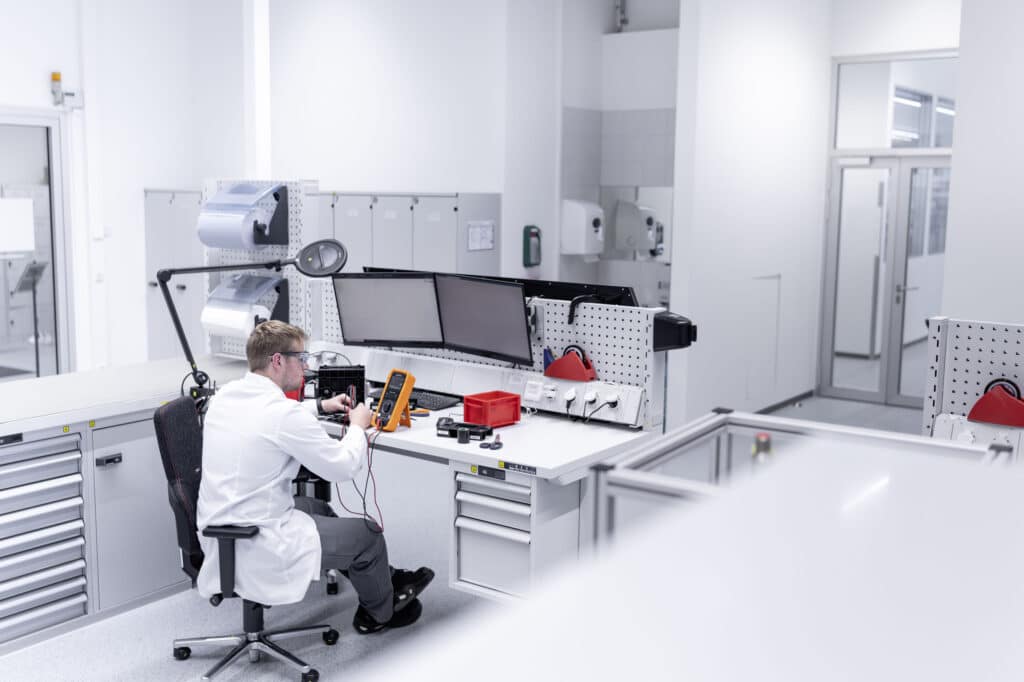 Technician testing electronics at a workstation in a modern laboratory with multiple monitors and testing equipment.