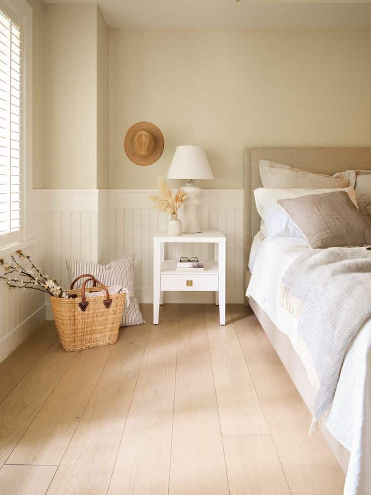 Cozy bedroom with neutral decor, light wooden flooring, bedside table, and wicker basket for a serene atmosphere.