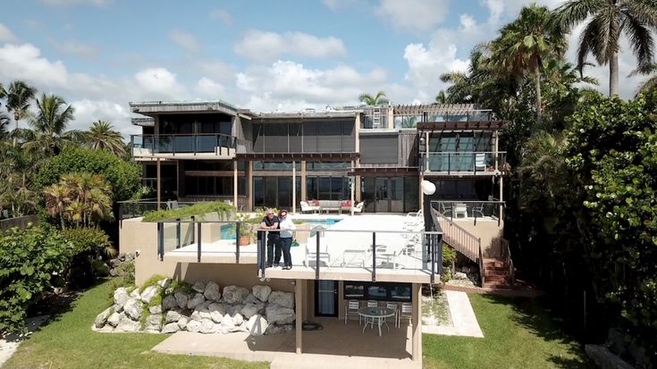 Adapting to climate change is going to cost Florida a lot_ Whos going to pay for it_ Modern beachfront house with spacious terrace, surrounded by palm trees and lush greenery under a clear blue sky. | Sky Rye Design Modern beachfront house with spacious terrace, surrounded by palm trees and lush greenery under a clear blue sky.