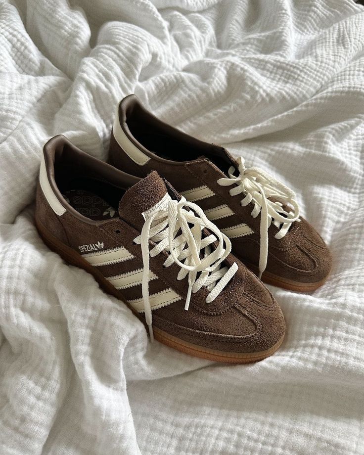 Brown suede sneakers with white stripes and laces on a soft, textured blanket, showcasing casual style and comfort.
