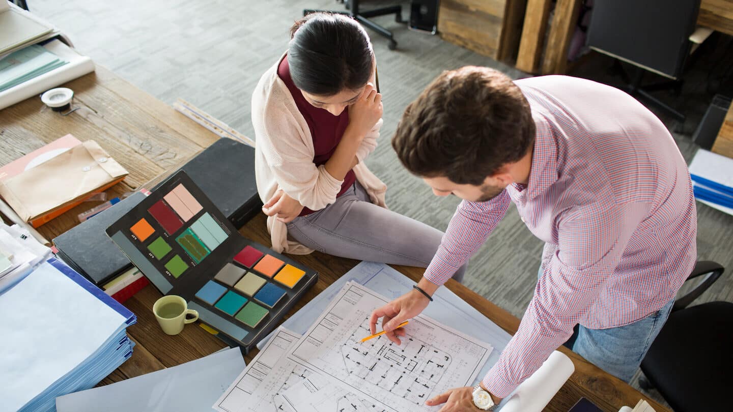 Architects reviewing blueprints and color samples in office; collaboration on design project with materials and plans spread across the table.