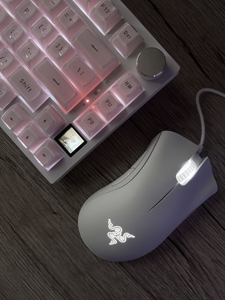 White gaming keyboard and mouse with RGB lighting on a wooden desk, featuring soft pink and white glows for an enhanced gaming setup.