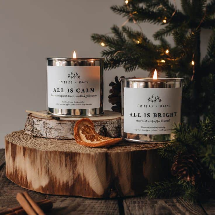 All Is Bright Soy Wax Candle Festive candles labeled All Is Calm and All Is Bright on a wooden stand with oranges, enhancing cozy holiday decor beside a lit tree. | Sky Rye Design Festive candles labeled All Is Calm and All Is Bright on a wooden stand with oranges, enhancing cozy holiday decor beside a lit tree.