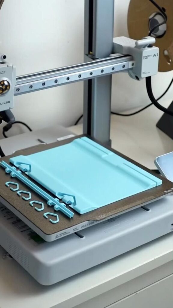 4a5c9f32e1c123df862028d050b632b3 3D printer creating light blue objects on a build plate, showcasing advanced manufacturing technology. | Sky Rye Design 3D printer creating light blue objects on a build plate, showcasing advanced manufacturing technology.