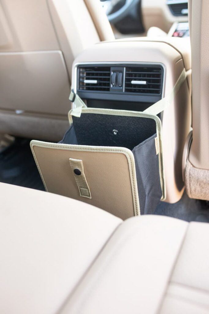 Car backseat organizer with strap, hanging from tan seat, ideal for tidy storage in vehicles.