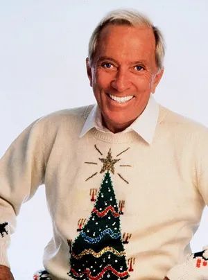 Andy Williams - Christmas Smiling person in Christmas sweater with decorated tree design, white background, festive holiday attire. | Sky Rye Design Smiling person in Christmas sweater with decorated tree design, white background, festive holiday attire.