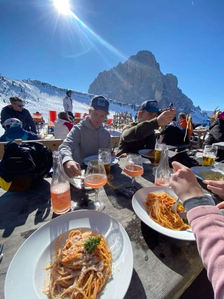 Outdoor dining with spaghetti at a snowy mountain café, sunlight and blue sky. Ideal winter getaway with food and stunning views.