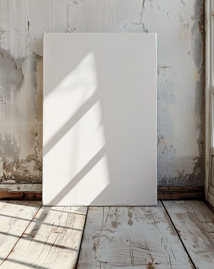 Blank canvas against a rustic wall with sunlight casting shadows on wooden floor. Perfect for art or interior design themes.