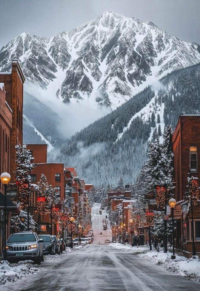 Snowy mountain view over a decorated street with cars in a winter town scene.