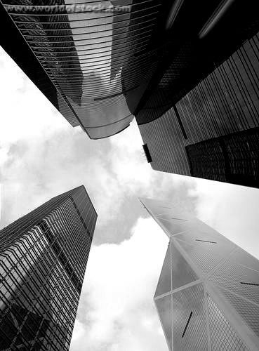 Dramatic upward view of modern skyscrapers in black and white, showcasing architectural design and urban skyline against a cloudy sky.