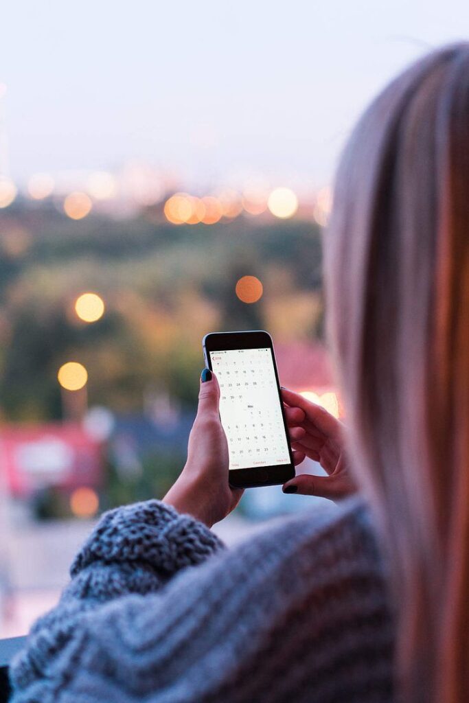 Best Free Images for 2025 _ Page 5 of 79 _ picjumbo Person checking smartphone calendar at sunset, outdoor blurred city view in background. | Sky Rye Design Person checking smartphone calendar at sunset, outdoor blurred city view in background.