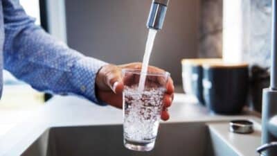 Person filling glass with fresh tap water in a modern kitchen setting.