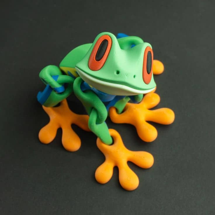 Colorful toy frog figurine with big orange feet and vibrant eyes on a dark background. Playful and fun children's decoration.