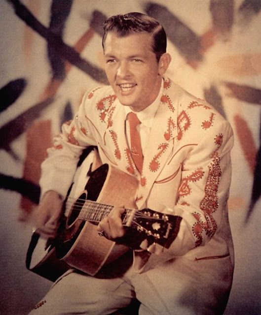 Bobby Helms_ 1957 Man in embroidered suit playing guitar, retro style backdrop. Vintage music performance vibe. | Sky Rye Design Man in embroidered suit playing guitar, retro style backdrop. Vintage music performance vibe.