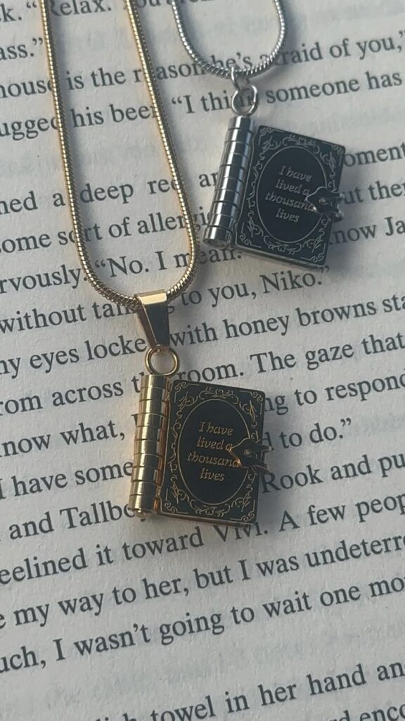 Bookish Necklace _ Bookish Pendent _ Book Lover Gift _ Bookish _ I have lived a thousand lives _ Locket _ Bookish Locket Book-shaped gold and silver pendants on a page, engraved with I have lived a thousand lives, symbolizing the magic of reading. | Sky Rye Design Book-shaped gold and silver pendants on a page, engraved with I have lived a thousand lives, symbolizing the magic of reading.