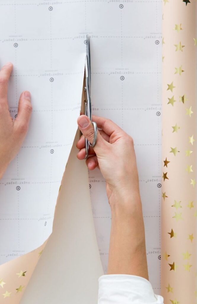 Brian and Anissa Zajacs Cottage House Is as Cozy as It Gets Person cutting star-patterned wrapping paper with scissors, focusing on precision and craft. | Sky Rye Design Person cutting star-patterned wrapping paper with scissors, focusing on precision and craft.