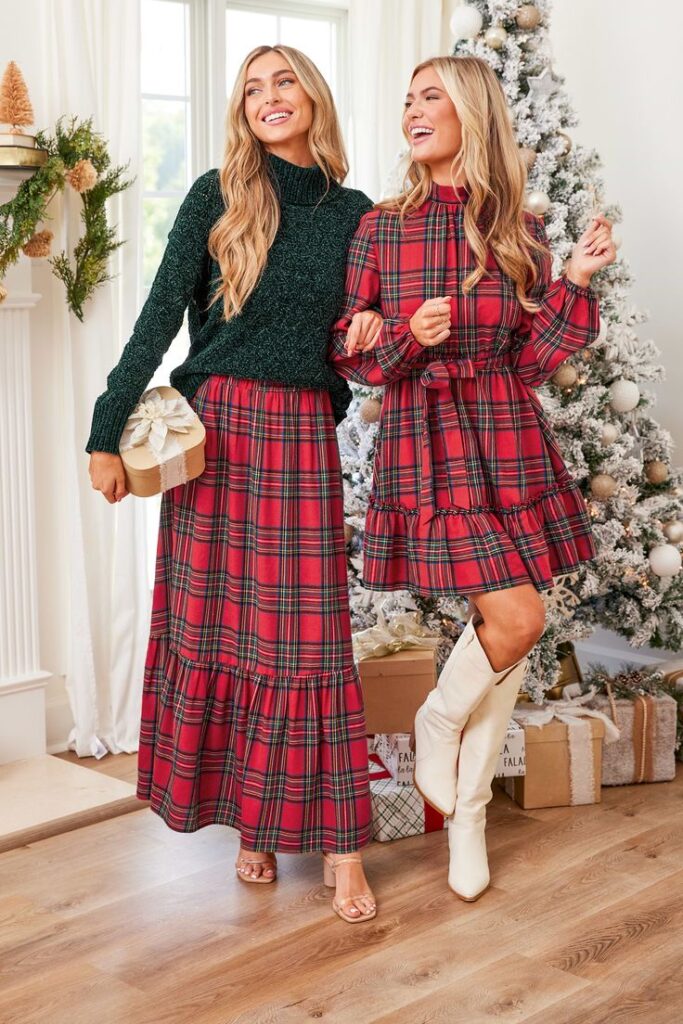 Burgundy Plaid Ruffled Maxi Skirt Two women smiling in festive plaid outfits beside a decorated Christmas tree with wrapped presents. | Sky Rye Design Two women smiling in festive plaid outfits beside a decorated Christmas tree with wrapped presents.