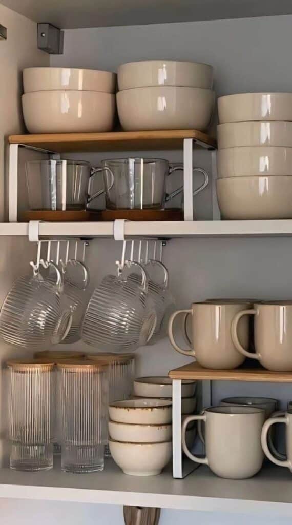 Organized kitchen cabinet with neatly stacked bowls, mugs, and glasses, showcasing efficient use of space and stylish storage solutions.