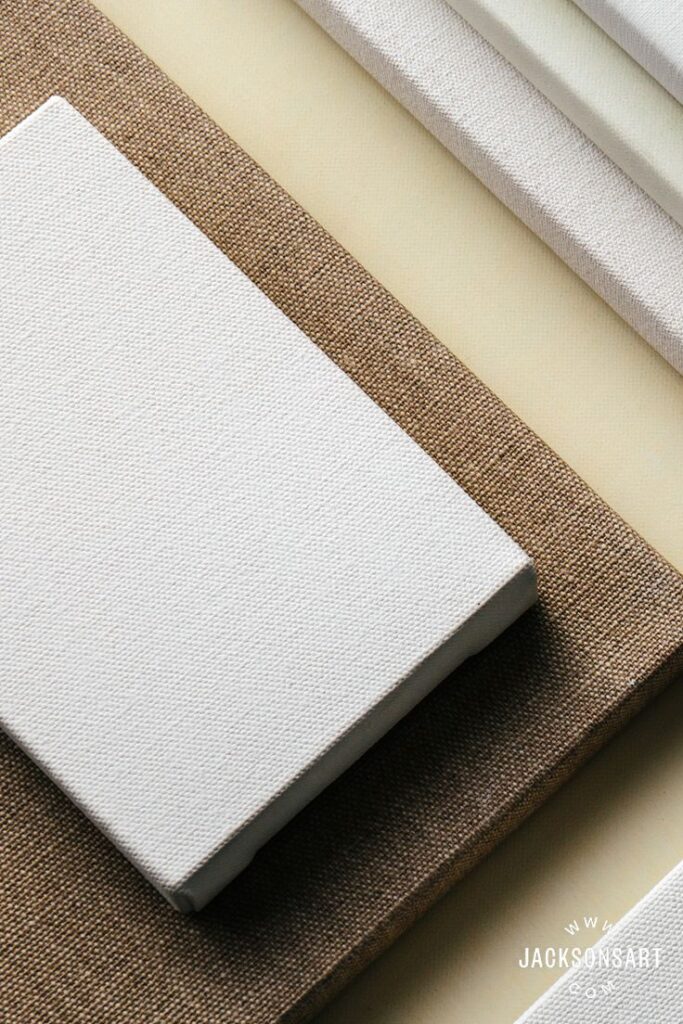 Stacked blank canvases on a beige surface, showcasing different textures and types for art projects.