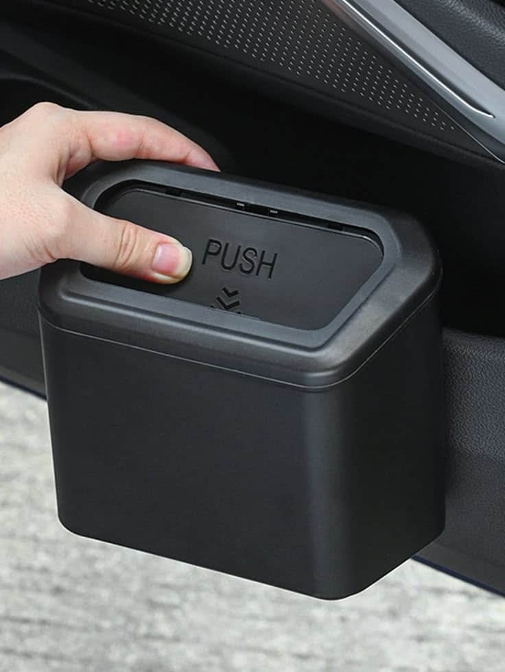 Hand pushing lid on black car trash bin for convenient waste disposal. Ideal for vehicle interior organization.