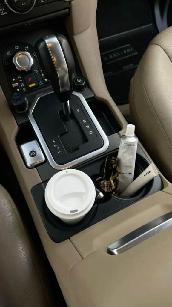 Car interior with gear shift, coffee cup, hand cream, and sunglasses in the cup holder.