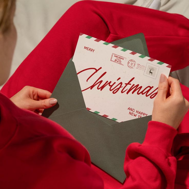 Person in cozy attire holding festive Christmas card in green envelope, celebrating holiday spirit.