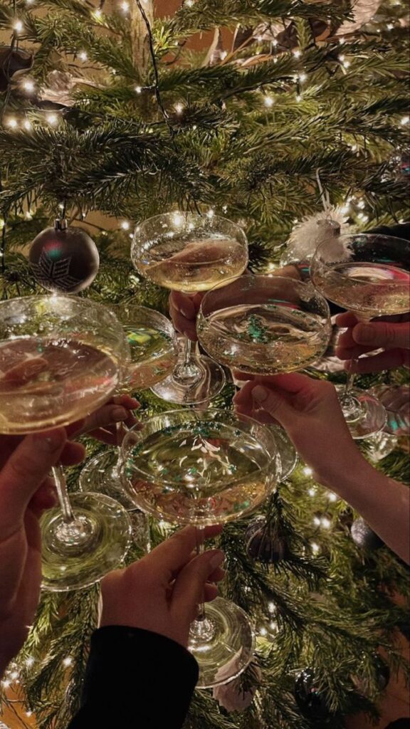 Hands raising champagne glasses in a toast by a decorated Christmas tree with glowing lights.