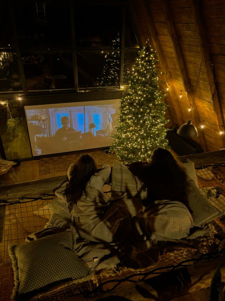 Cozy attic movie night with Christmas tree, projector screen, and two people in blankets.