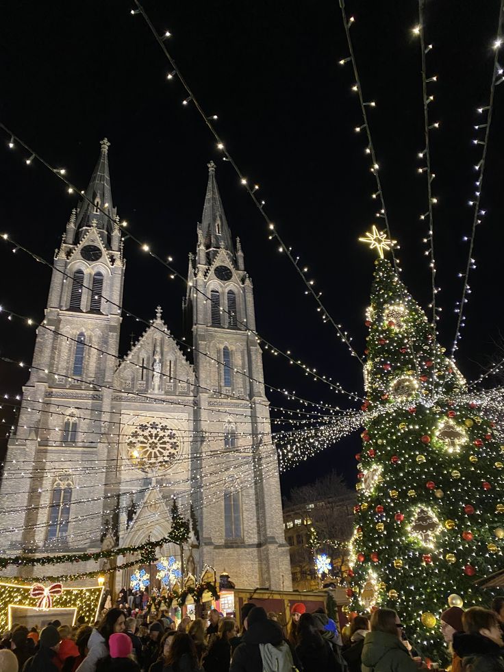 Festive Christmas market with a lit-up cathedral and decorated tree, nighttime celebration, people enjoying holiday spirit.