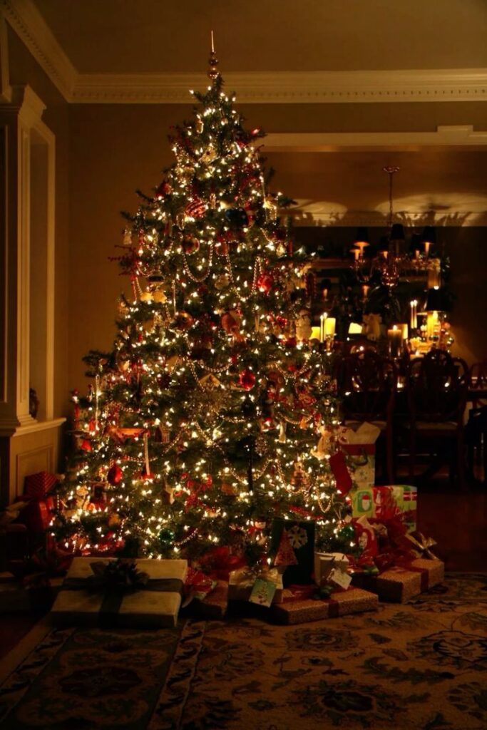 Decorated Christmas tree with lights and presents in a warmly lit living room.