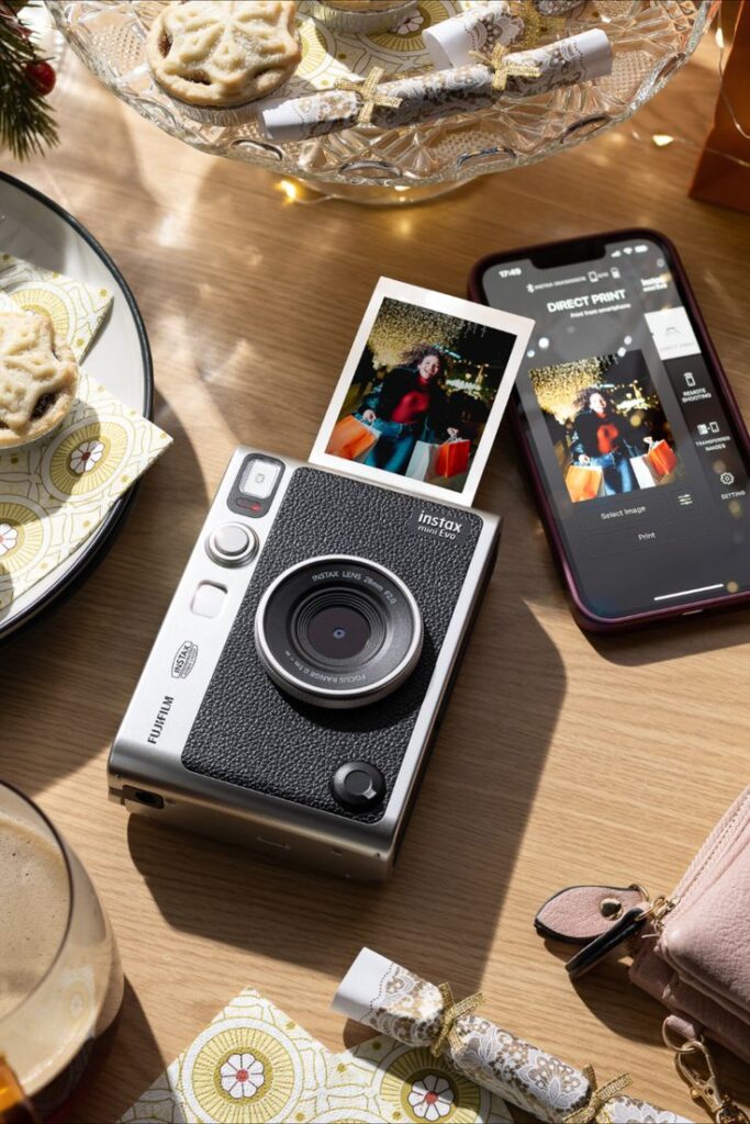 Christmas with the instax mini Evo Instax Mini Evo camera on table capturing festive moments, with a smartphone nearby, Christmas treats, and holiday decor in the background. | Sky Rye Design Instax Mini Evo camera on table capturing festive moments, with a smartphone nearby, Christmas treats, and holiday decor in the background.