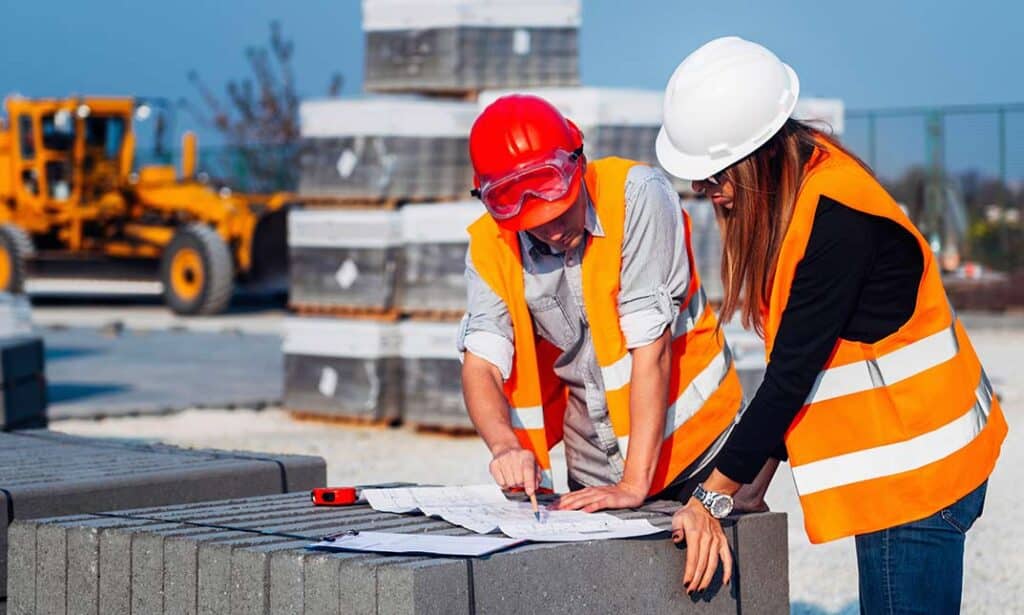 Construction-Cost-Estimating-and-Cost-Control-1-1024x615 Construction workers in safety vests and helmets discussing blueprints on site with machinery in background. | Sky Rye Design Construction workers in safety vests and helmets discussing blueprints on site with machinery in background.