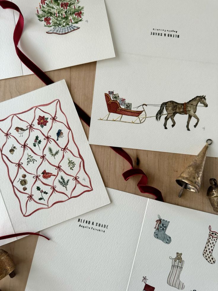 Festive holiday cards featuring Christmas tree, sleigh, stockings, and birds, accompanied by a red ribbon and bells on a wooden table.