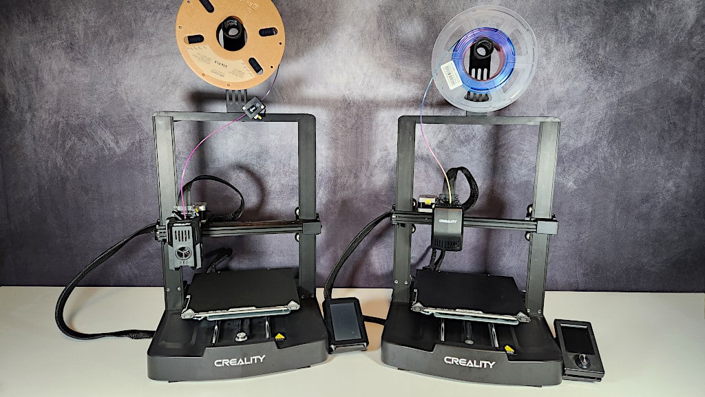 Two Creality 3D printers with filament spools, set against a gray background.