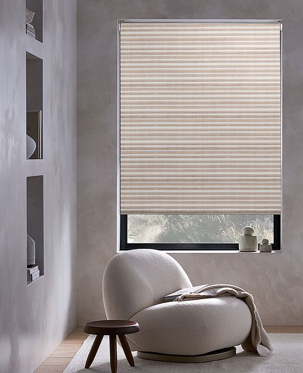 Modern living room with a cozy white chair, small table, and beige window blinds filtering light, creating a serene atmosphere.