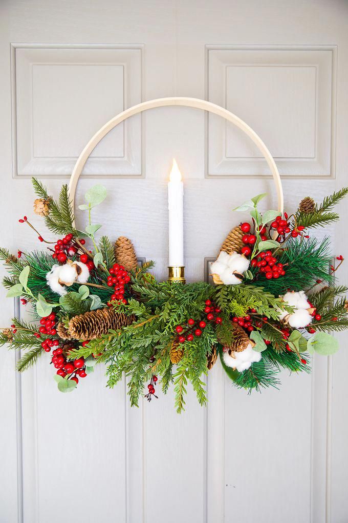 DIY Embroidery Hoop Christmas Wreath Festive holiday wreath with greenery, pinecones, berries, and a lit candle on a light gray door. | Sky Rye Design Festive holiday wreath with greenery, pinecones, berries, and a lit candle on a light gray door.