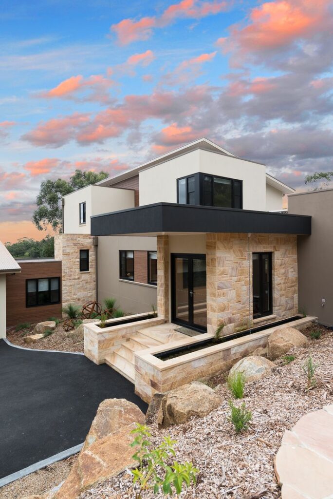 DPE House Design Studio - Energy Efficient Sustainable House Design_Custom Home House Design_Solar Solutions Design_House Plans_ DPE house Design Studio_Melbourne_Victoria_Australia Modern two-story house with stone facade and flat roof under a vibrant, sunset sky. | Sky Rye Design Modern two-story house with stone facade and flat roof under a vibrant, sunset sky.