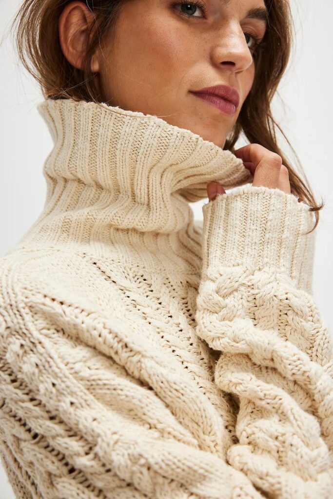Woman wearing cozy beige knit turtleneck sweater, looking sideways. Warm winter fashion style.