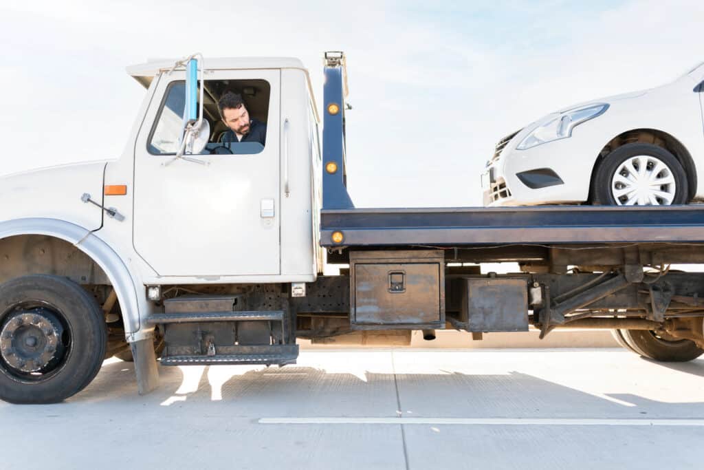 Tow truck driver on the road transporting a white car, focusing on safety and efficiency under a clear blue sky.